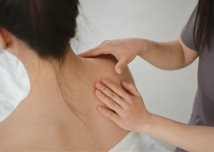 Hands applying therapeutic pressure to the shoulder and upper back during a chiropractic care session.