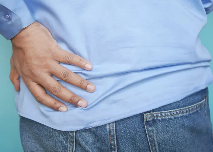 Person placing a hand on the lower back or hip area, indicating pain or discomfort.