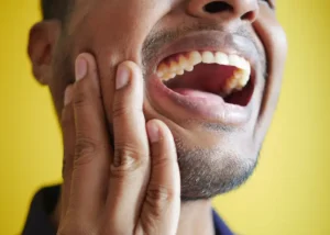 Person holding their cheek with a pained expression, indicating jaw pain or TMJ discomfort.