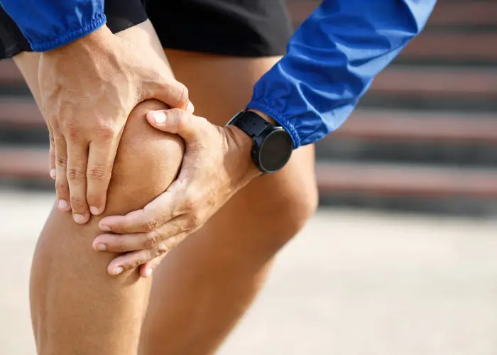 Person holding their knee with both hands, showing signs of knee pain during outdoor activity.