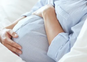 Pregnant person resting hands on their belly while lying down, representing prenatal care and pregnancy support.