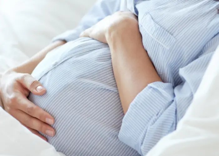 Pregnant person resting hands on their belly while lying down, representing prenatal care and pregnancy support.