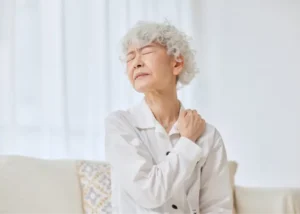 Older adult holding their shoulder with a tense expression, indicating shoulder pain or discomfort.
