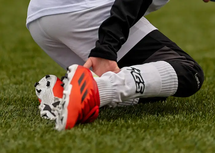 Person kneeling on grass and holding their ankle, indicating a sports‑related injury or strain.