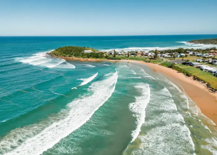 Aerial coastal view of Arrawarra with turquoise waves, sandy shoreline and nearby homes.