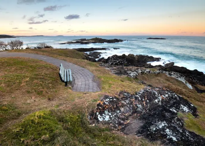 Coastal sunset scene near Bonville with rocky shoreline, ocean waves and walking path.