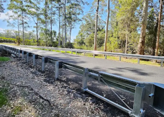 Rural roadside in Bucca with metal guardrail, tall trees and dense forest vegetation.