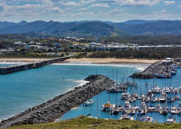 Aerial view of the Coffs Harbour marina with boats, breakwalls, beach and surrounding township.