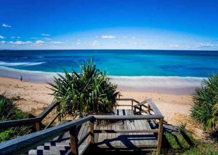 Beach staircase leading to Corindi Beach with turquoise water and clear sky.