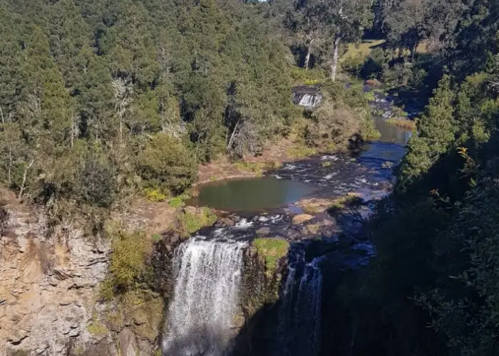 Waterfall in Megan surrounded by forest, rocky cliffs and lush greenery.