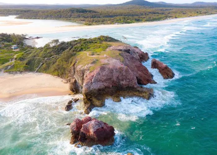 Coastal view of Red Rock headland with waves, rocky cliffs and surrounding greenery.