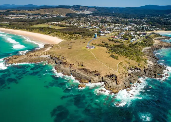 Aerial view of Woolgoolga headland with lighthouse, rocky coastline and nearby beach.